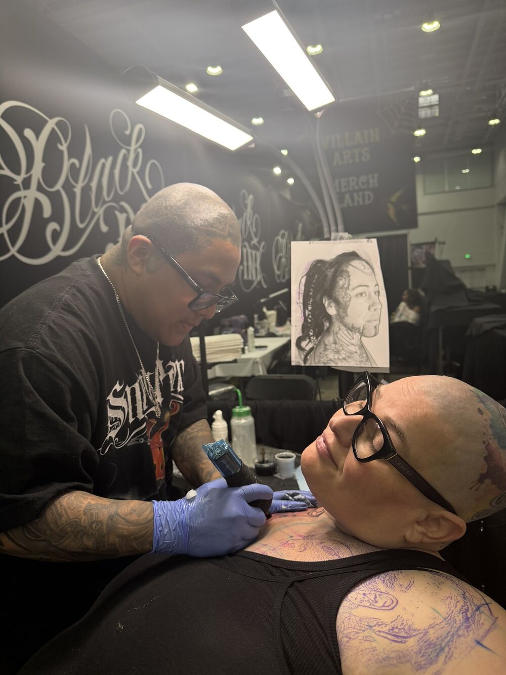 An artist in a studio tattooing a client's neck while the client rests calmly