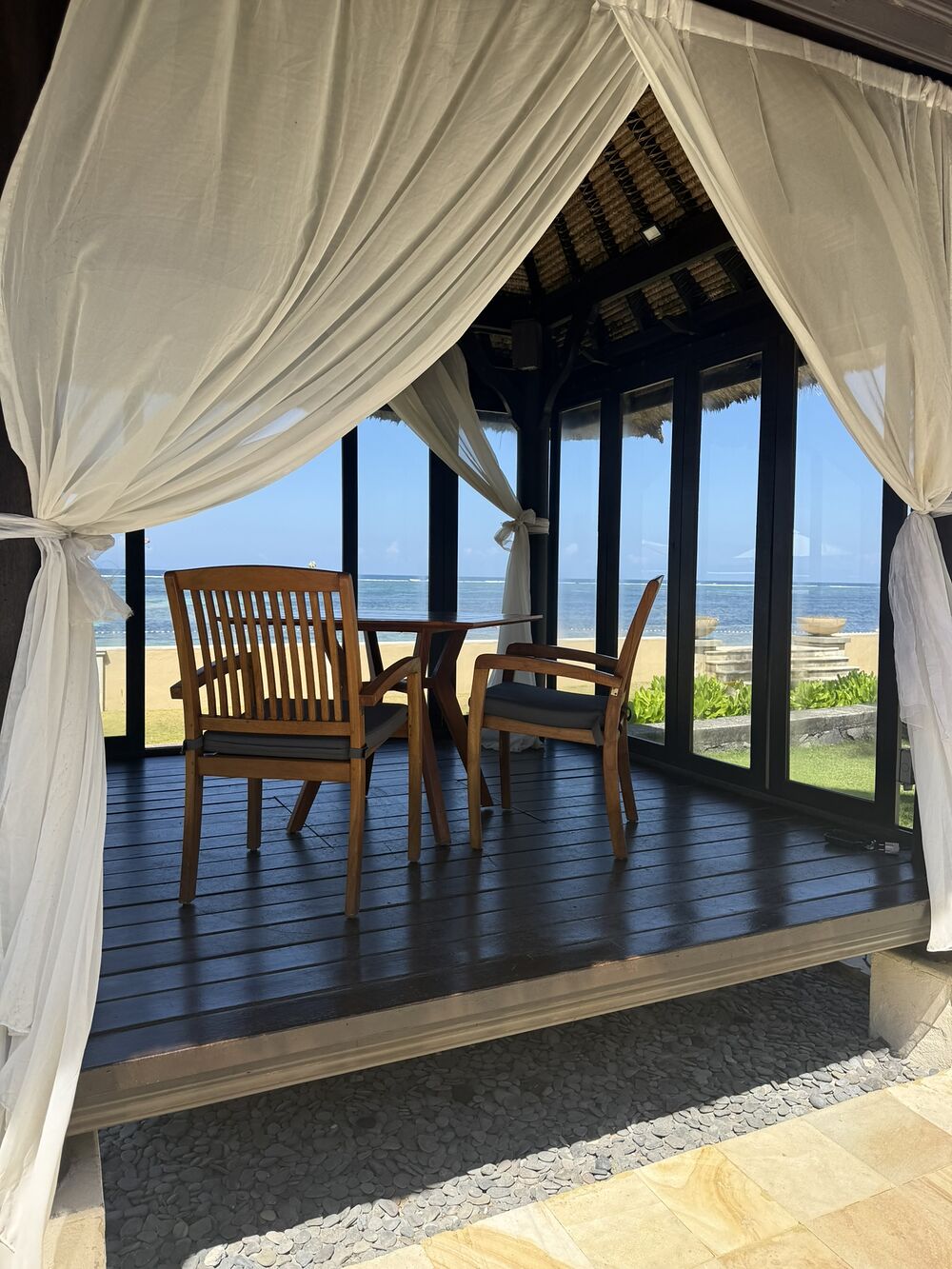 A private open-air pavilion with white curtains and teak chairs